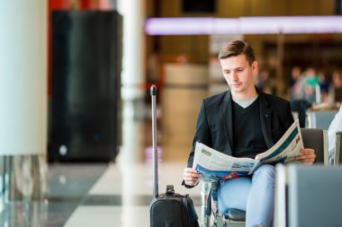Gazete yatılı için beklerken havaalanında genç beyaz adamla. Elbise giyen sıradan genç işadamı.