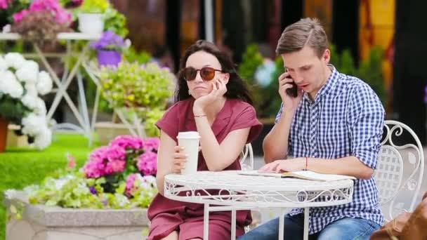 Restaurante turistas pareja en la cafetería al aire libre. Chica joven está enojado con su novio porque él está ocupado con las tareas — Vídeos de Stock