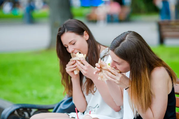 Mulheres caucasianas comem sanduíche de hambúrguer fast food na rua ao ar livre. Meninas ativas com fome e comer comida de rua após longa caminhada — Fotografia de Stock