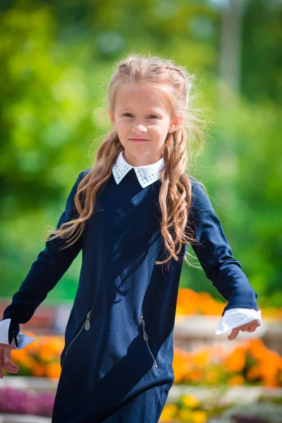 Jolie petite fille qui frappe et pose devant son école le 1er septembre. Adorable petit enfant se sentant très excité de retourner à l'école — Photo