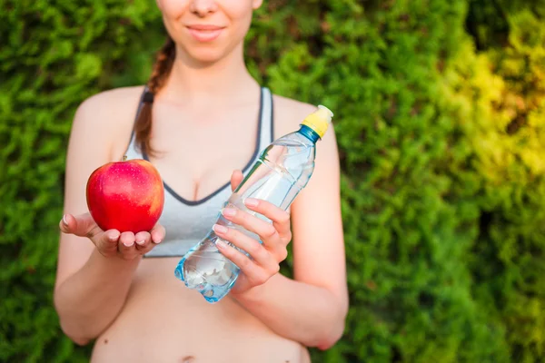 Young woman with apple and bottle of water after running outside. Female fitness model training outside in the park. Healthy wellness fitness lifestyle. — Stock Photo, Image