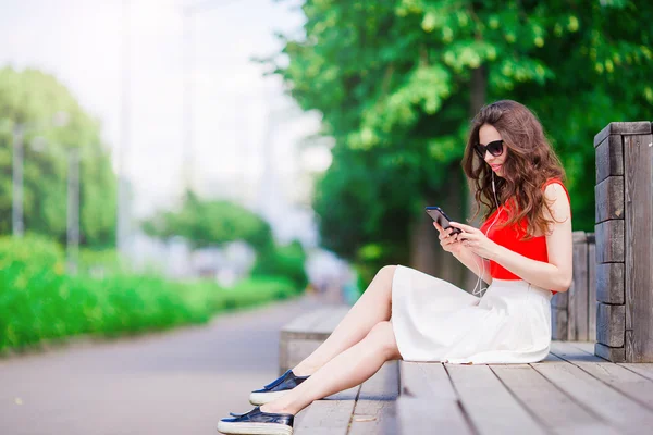 Mooi meisje luisteren muziek door smartphone op zomervakantie. Jonge aantrekkelijke toeristische met mobiele telefoon buitenshuis genieten van vakantie. — Stockfoto