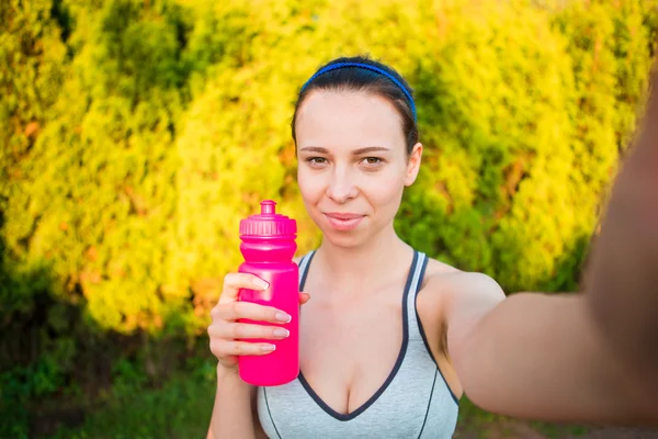 Junge Frau mit Wasserflasche, nachdem sie nach draußen gelaufen war. Weibliche Fitness-Models trainieren draußen und machen Selfies im Park. Gesunder Wellness Fitness Lebensstil. — Stockfoto