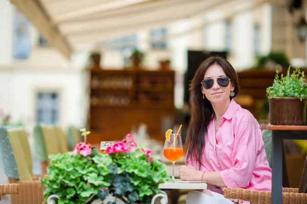 Retrato de una joven hermosa mujer sentada en un café al aire libre bebiendo sabroso cóctel. Turista feliz disfrutar de vacaciones europeas en restaraunt al aire libre —  Fotos de Stock