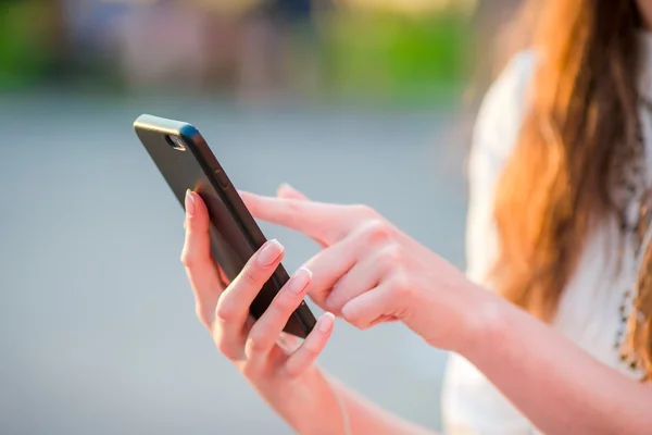 Gros plan de mains féminines tient le téléphone portable à l'extérieur dans la rue dans les lumières du soir. Femme utilisant un smartphone mobile . — Photo