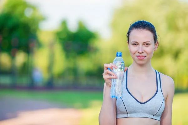 Young woman with bottle of water after running outside. Female fitness model training outside in the park. Healthy wellness fitness lifestyle. — Stock Photo, Image