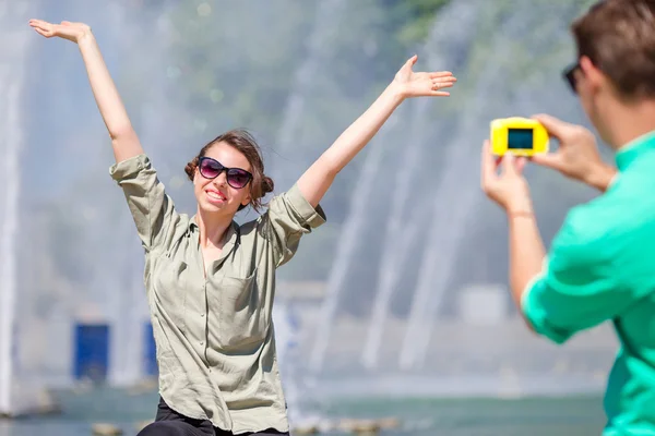 Fidanzato scattare una foto della sua ragazza mentre seduto sullo sfondo della fontana. Giovane uomo che fa foto di donna per strada ridendo e divertendosi in estate . — Foto Stock
