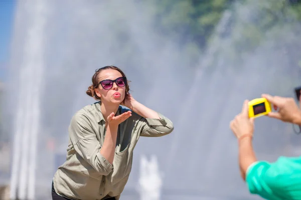 Novio tomando una foto de su amigo mientras estaba sentado detrás de la fuente. Joven hombre haciendo foto de mujer en la calle riendo y divirtiéndose en verano . —  Fotos de Stock