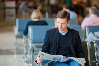 Gazete yatılı için beklerken havaalanında genç beyaz adamla. Elbise giyen sıradan genç işadamı.