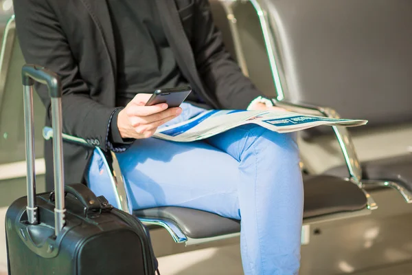 Unga kaukasiska man med tidningen och cellphone på flygplatsen i väntan på ombordstigning. Casual ung affärsman bära kavaj. — Stockfoto