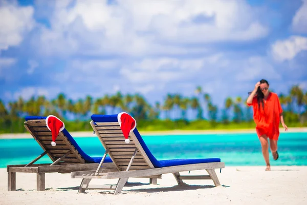 Due lettini con Babbo Natale rosso sulla spiaggia tropicale bianca con acqua turchese. Giovane donna che cammina sulla spiaggia — Foto Stock