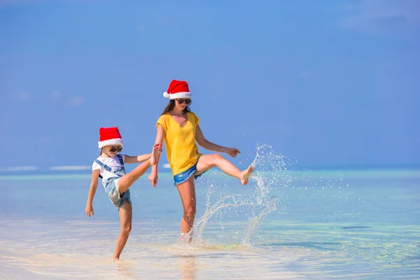 Plaj tatili sırasında Santa Şapkalı küçük bir kız ve genç bir anne. — Stok fotoğraf