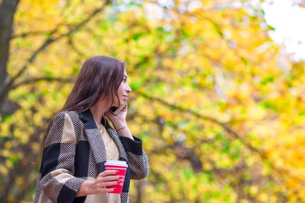 快乐美丽的女人，在下秋天的落叶的秋天公园里喝咖啡 — 图库照片