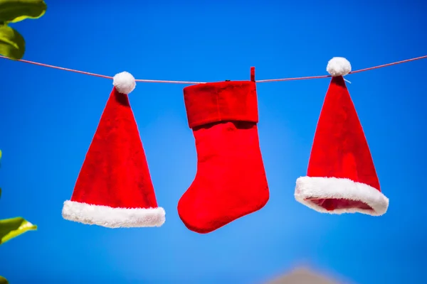 Red Santa hats and Christmas stocking hanging on tropical beach between palm trees — Stock Photo, Image