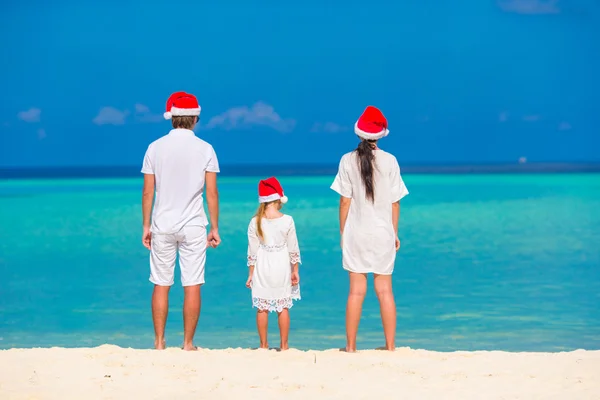 Ung familie i nissehatter som slapper av på tropisk strand i juleferien – stockfoto