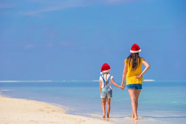 Plaj tatili sırasında Santa Şapkalı küçük bir kız ve genç bir anne. — Stok fotoğraf