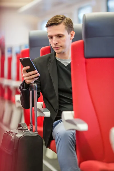 Young man traveling by train. Tourist writing a message on cellphone while traveling by express train — Stock Photo, Image