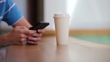 Kafede cep telefonu ve bir bardak kahve tutan erkeklerin yakın çekimi. Cep telefonu kullanan bir adam. Çocuk zeka ekranına dokunuyor. Bulanık arkaplan, yatay.