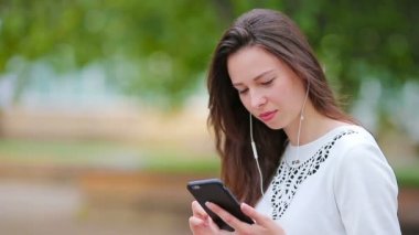 Kafkasyalı genç bir kadın parktaki akıllı telefonuyla mesaj yolluyor. Güneş gözlüklü güzel kız ahşap bankta akıllı telefon kullanarak oturuyor.