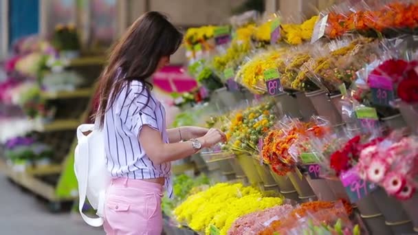 Beautiful young woman with long hair selecting fresh flowers at european market — Stock Video