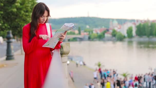 Счастливая молодая женщина с картой города на фоне знаменитого моста в Европе. Туристическая женщина с картой на улице во время отдыха в Европе . — стоковое видео