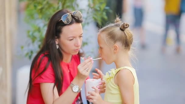 若い母親と娘は屋外でアイスクリームを食べています。ママは娘のアイスクリームを路上で食べる — ストック動画