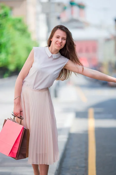 Joven chica feliz con bolsas de compras coger un taxi. Retrato de una hermosa mujer feliz parada en la calle sosteniendo bolsas de compras sonriendo y cogiendo un taxi —  Fotos de Stock