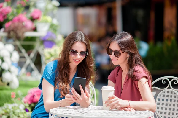 Twee jonge meisjes in het café. Twee vrouwen na het winkelen met tassen zitten in openlucht cafe met koffie en met behulp van smartphone — Stockfoto