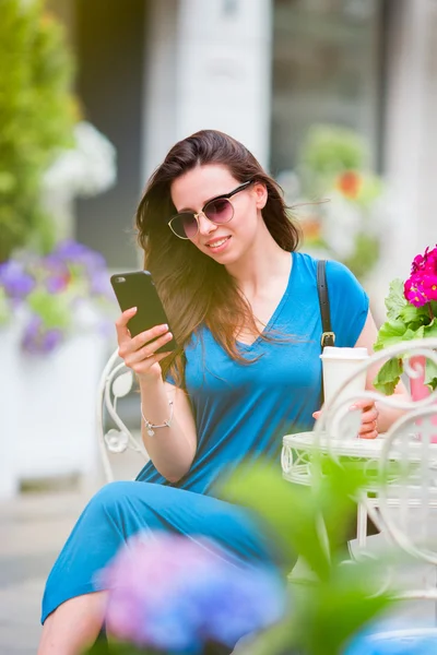 Portret van jonge mooie vrouw zittend in outdoor café koffie drinken en smartphone gebruiken. — Stockfoto