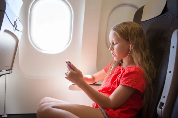 Entzückendes kleines Mädchen, das mit dem Flugzeug unterwegs ist. Kind hört Musik am Flugzeugfenster — Stockfoto