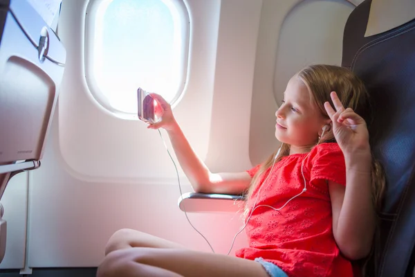 Entzückendes kleines Mädchen, das mit dem Flugzeug unterwegs ist. Kind hört Musik am Flugzeugfenster — Stockfoto