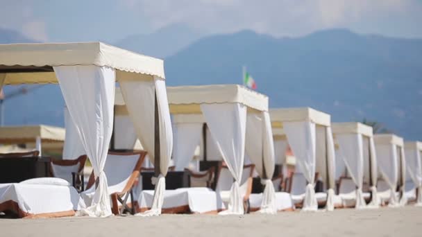 Tumbonas de madera frente a un mar turquesa a la luz de la tarde. Tumbonas en la famosa playa de arena italiana en Forte dei Marmi — Vídeos de Stock
