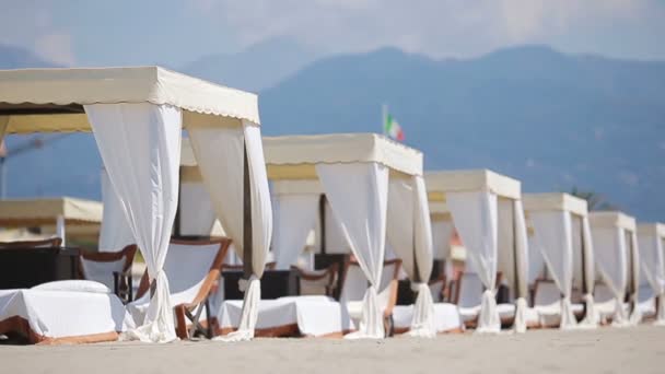 Camas de sol de madeira em frente a um mar azul-turquesa na luz da noite. Camas de sol na famosa praia de areia italiana no Forte dei Marmi — Vídeo de Stock