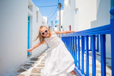 Eski sokaklarda açık havada beyaz elbiseli büyüleyici kız bir Mikonos. Yunanistan'da Mikonos Adası'nda beyaz duvarları ve renkli kapıları ile tipik Yunan geleneksel köyün sokakta Çocuk