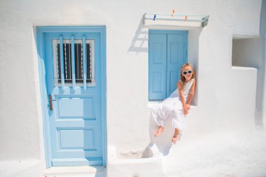 Eski sokaklarda açık havada beyaz elbiseli büyüleyici kız bir Mikonos. Yunanistan'da Mikonos Adası'nda beyaz duvarları ve renkli kapıları ile tipik Yunan geleneksel köyün sokakta Çocuk