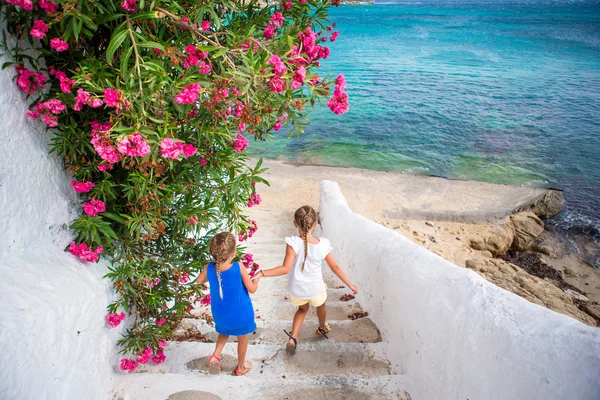 Dwie dziewczyny w niebieskie sukienki, zabawy na świeżym powietrzu. Dzieci ulicy typowej greckiej tradycyjnej wioski z białymi ścianami i kolorowe drzwi na wyspie Mykonos, Grecja — Zdjęcie stockowe
