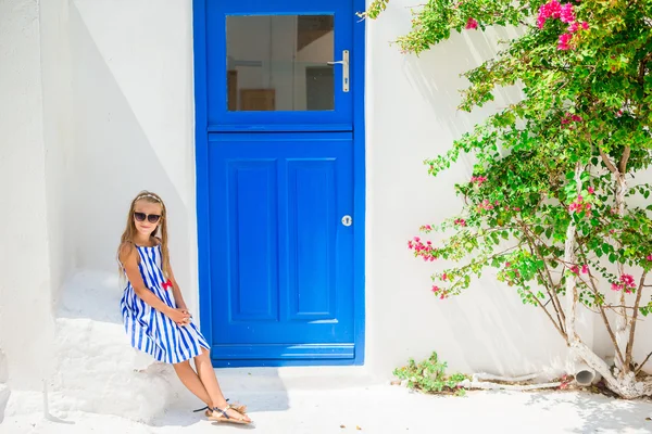 Roztomilá dívka v modrých šatech na ulici typické řecké tradiční vesnice s bílými stěnami a barevnými dveřmi na ostrově Mykonos, Řecko — Stock fotografie