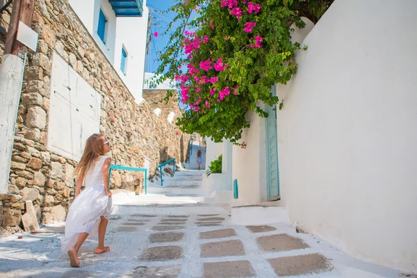 Adorable little girl in white dress having fun outdoors. Kid at street of typical greek traditional village with white walls and colorful doors on Mykonos Island, in Greece — Stock Photo, Image