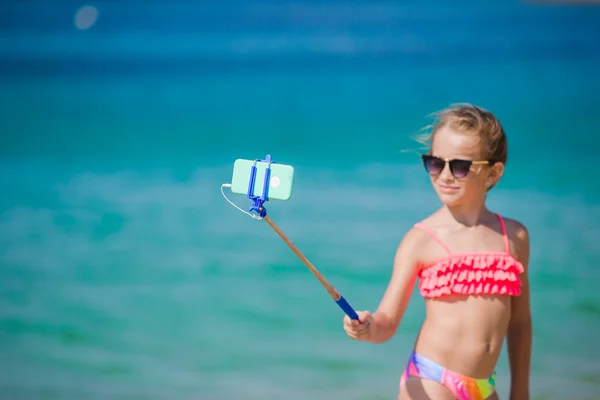 Маленькая девочка делает селфи-портрет со своим смартфоном на пляже. Очаровательная модель, создающая автопортретный фон красивого моря . — стоковое фото