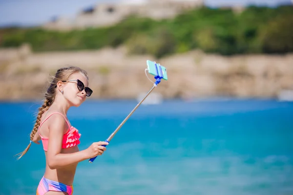 Meisje neemt zelfportret door haar smartphone op het strand. Kid genieten van haar suumer vakantie en maken foto's voor geheugen — Stockfoto