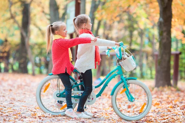 Two adorable girls in park at warm sunny autumn day. Kids on bicycle together — Stock Photo, Image