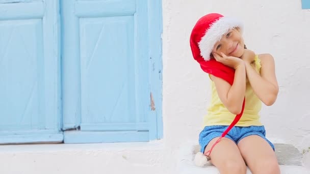 Niña con sombrero rojo al aire libre en la vieja calle en Mykonos. Niño en la calle del típico pueblo tradicional griego con paredes blancas y puertas coloridas en la isla de Mykonos, en Grecia — Vídeo de stock