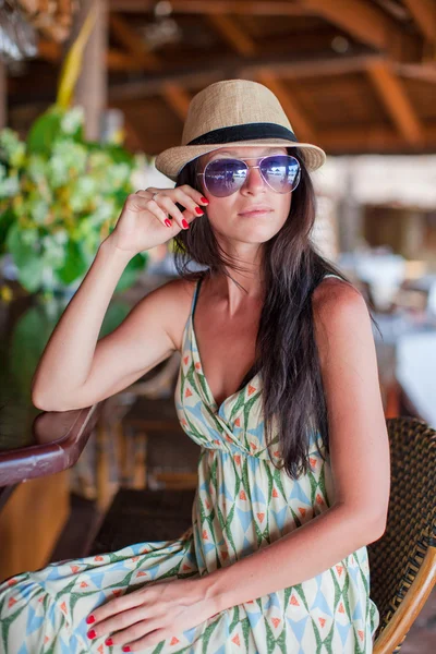 Beautiful brunette woman in long dress and hat relaxing in beach restaraunt — Stock Photo, Image