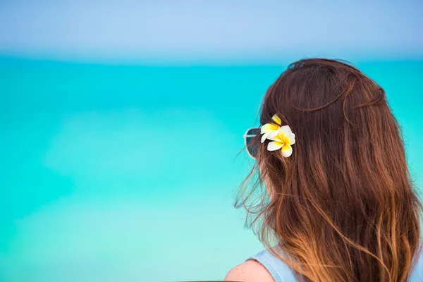 Młoda piękna kobieta podczas wakacje na tropikalnej plaży. Ciesz się suumer na urlop sam na plaży z frangipani kwiaty we włosach — Zdjęcie stockowe