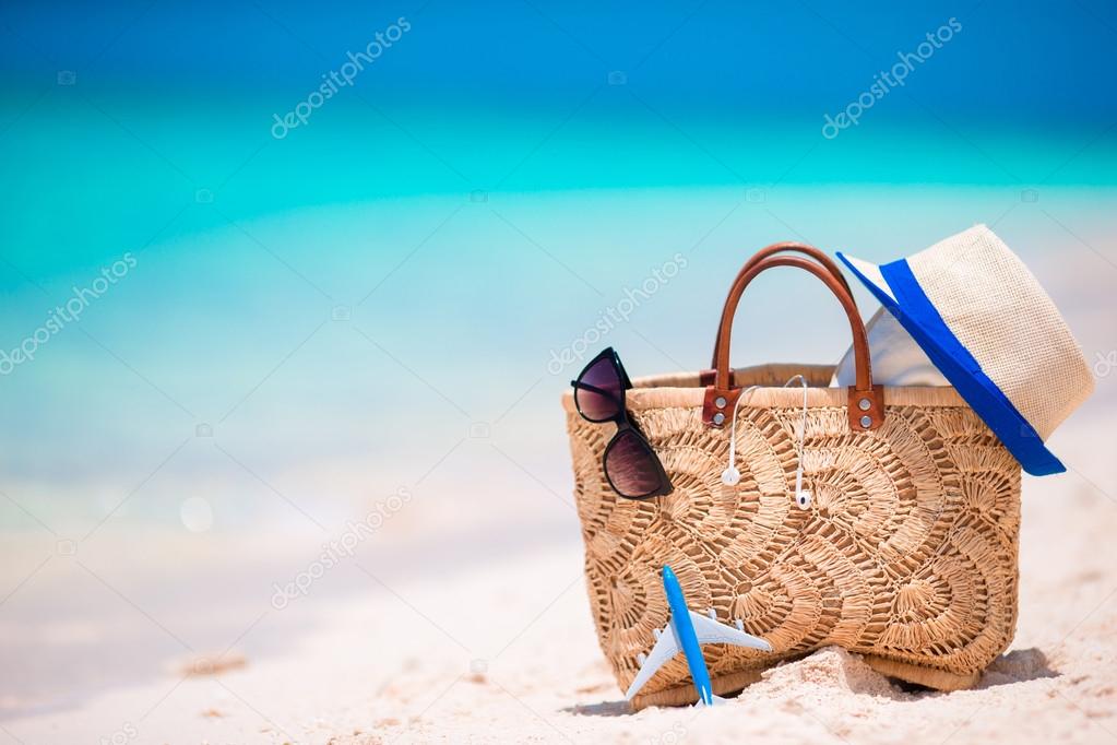 Beach accessories - straw bag, headphones, toy plane and sunglasses on the beach