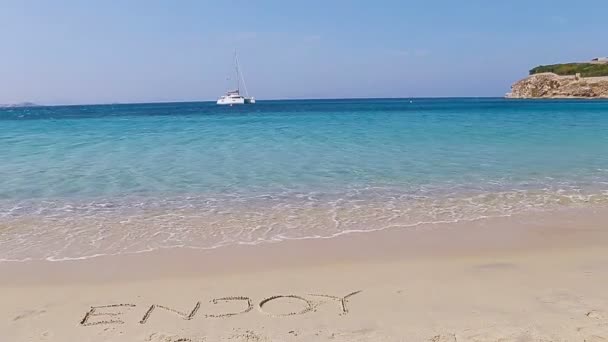 Word Enjoy handwritten on sandy beach with soft ocean wave on background. Idea for advertising — Stock Video