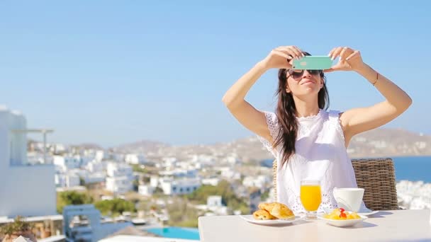 Kobieta przy Fotografia śniadanie przy użyciu mobilnych inteligentny telefon. Dziewczyna biorąc Zdjęcia żywności na luksusowe wakacje dla mediów społecznych. Piękna kobieta w ośrodku w Mykonos, Grecja. — Wideo stockowe