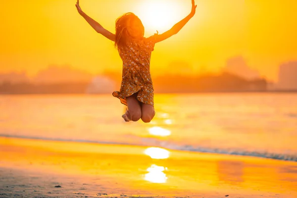 Schattig gelukkig klein meisje op wit strand bij zonsondergang. — Stockfoto