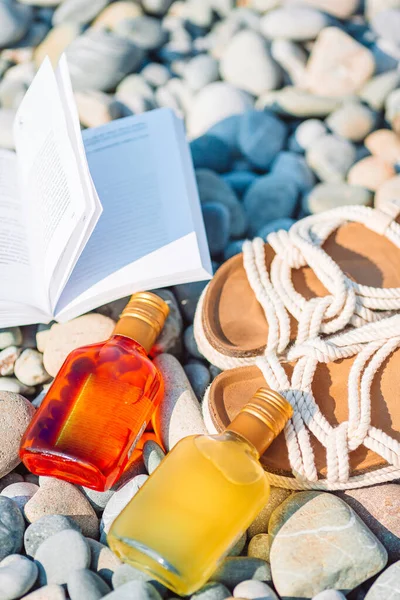Kapelusz plażowy na otwartej książce z filtrem przeciwsłonecznym i butami na żwirowej plaży — Zdjęcie stockowe