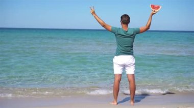 Mutlu adam sahilde eğleniyor ve karpuz yiyor.